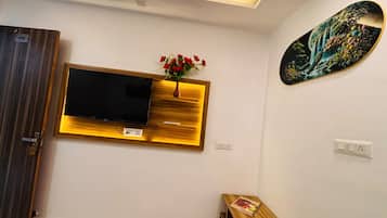 Une pièce avec un téléviseur fixé au mur, un banc en bois, une petite table avec un magazine et un tableau accroché au mur.