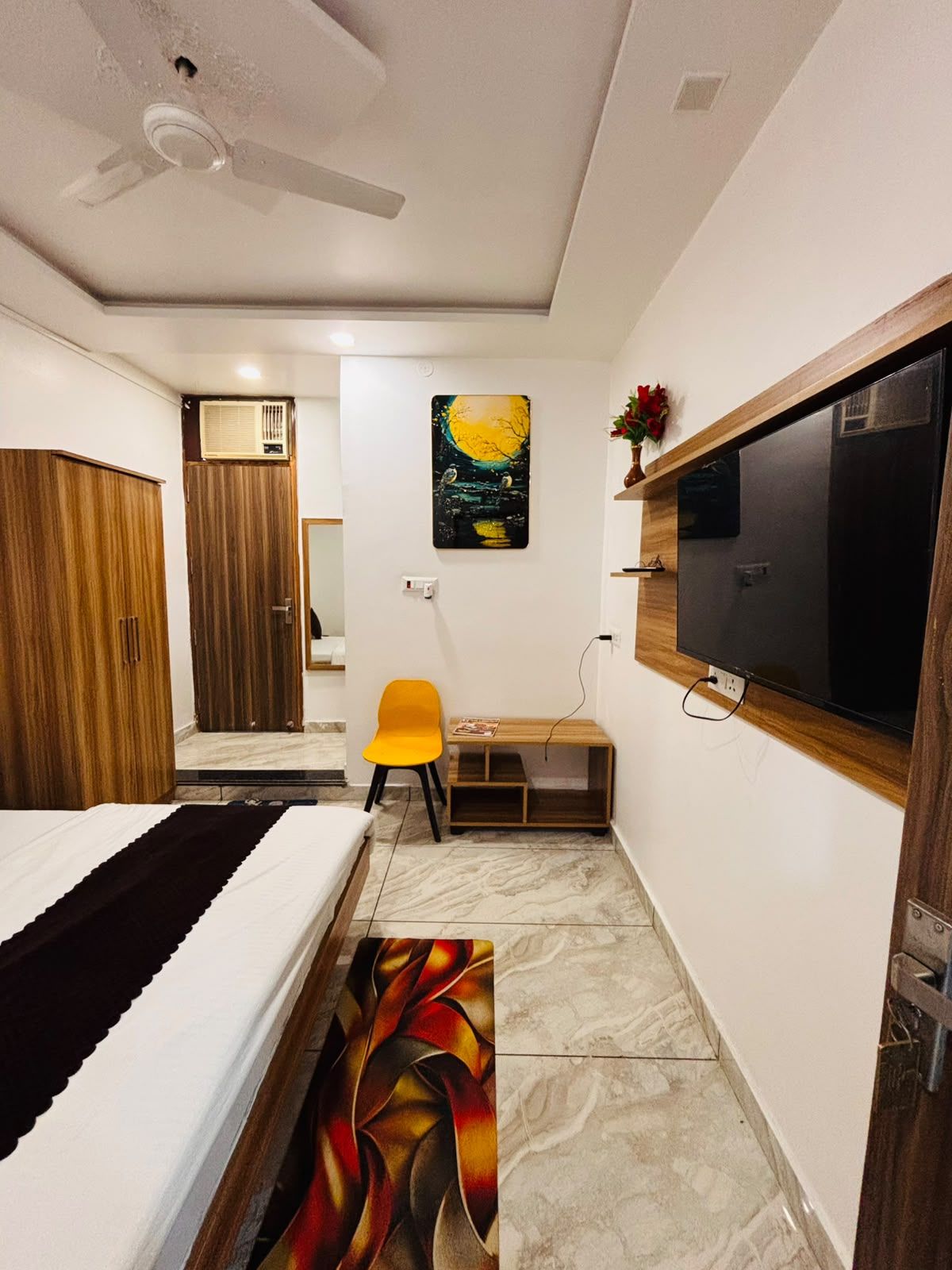 Une chambre à coucher comprenant un lit, un bureau, une chaise, un téléviseur et un ventilateur de plafond.