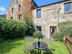 A stone building with ivy, a round table with chairs, and a bottle of wine. - Rooftops (Grange-over-Sands)