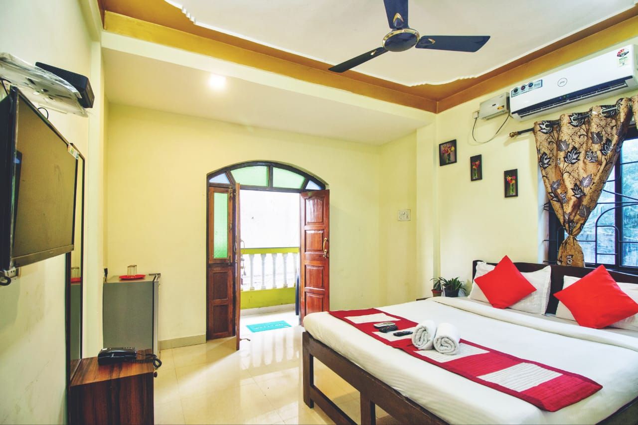 Une chambre d’hôtel équipée d’un lit, d’un ventilateur de plafond, d’un climatiseur, d’une télévision et d’une porte donnant sur un balcon.