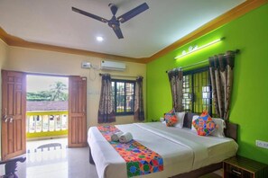 A hotel room with a bed, a ceiling fan, an air conditioning unit, and a view through an open door. - The Baga Beach 24in (Panaji)
