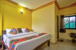A hotel room with two beds, a small table, a potted plant, and a window with curtains. - The Baga Beach 24in (Panaji)