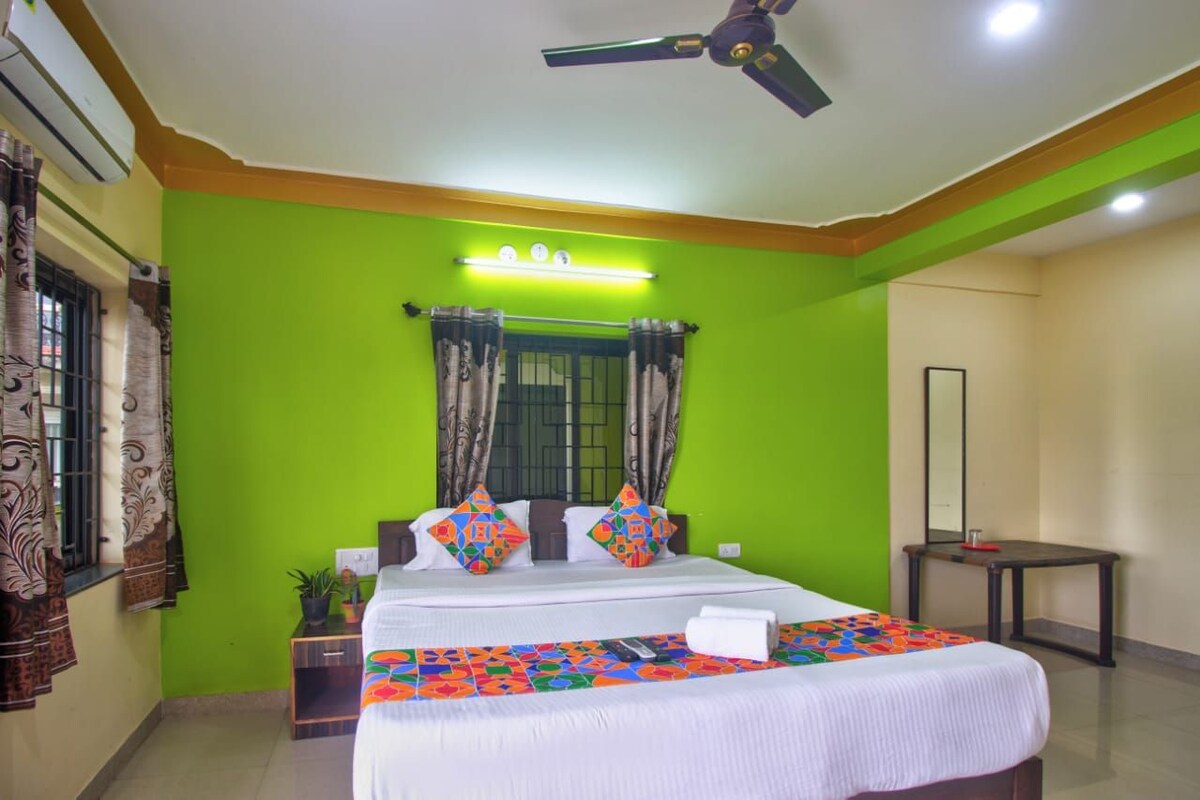 A hotel room with a bed, a ceiling fan, a nightstand, a bedside table, and a window with curtains.