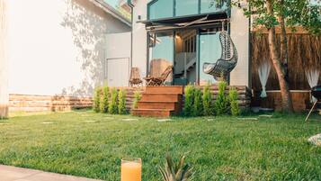 Un patio trasero con piscina, un muelle de madera, una mesa de comedor con fruta y jugo, y una casa con puerta de vidrio y mobiliario exterior.