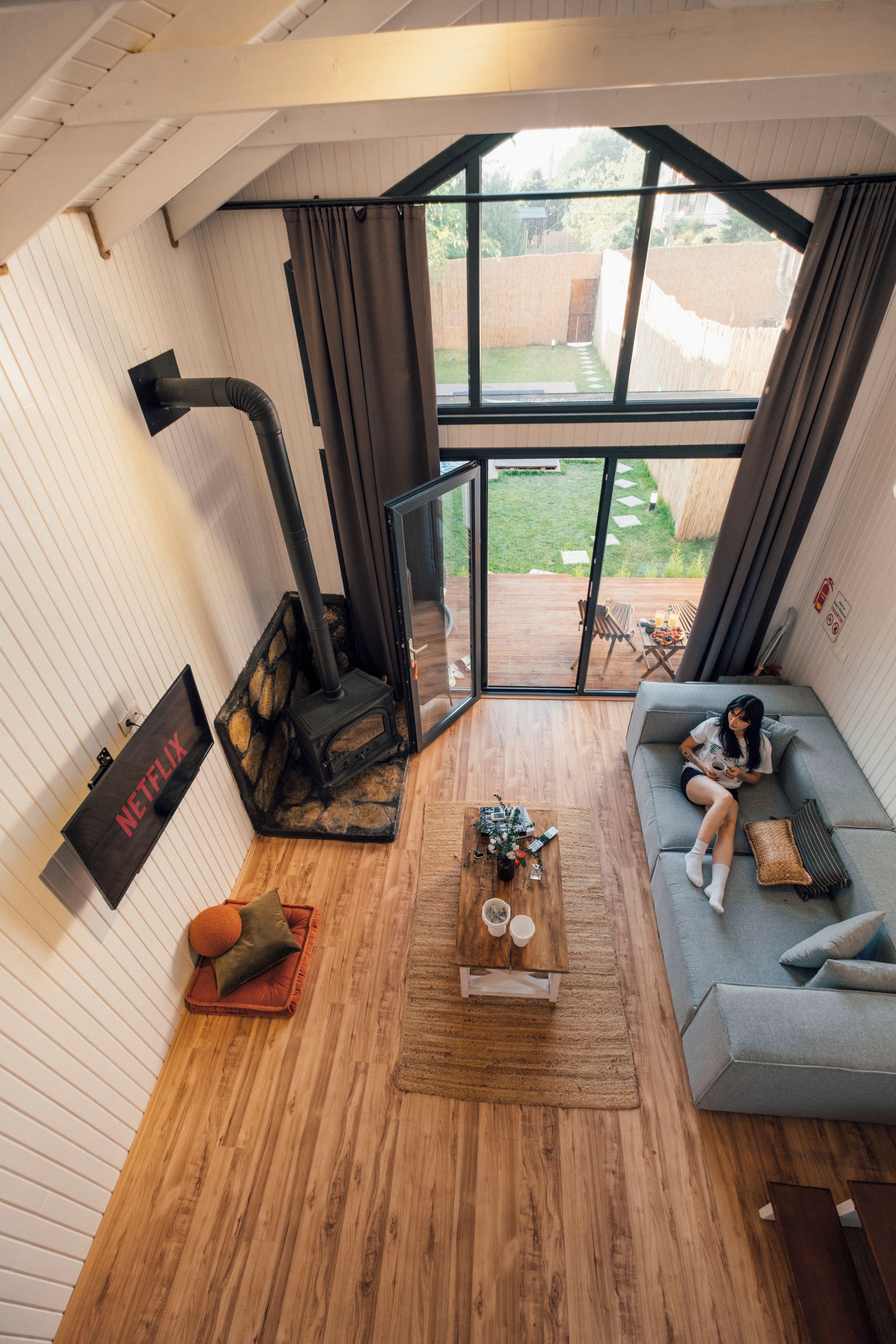 A modern living room with a stone fireplace, a sofa, a coffee table, and a large window overlooking a garden.