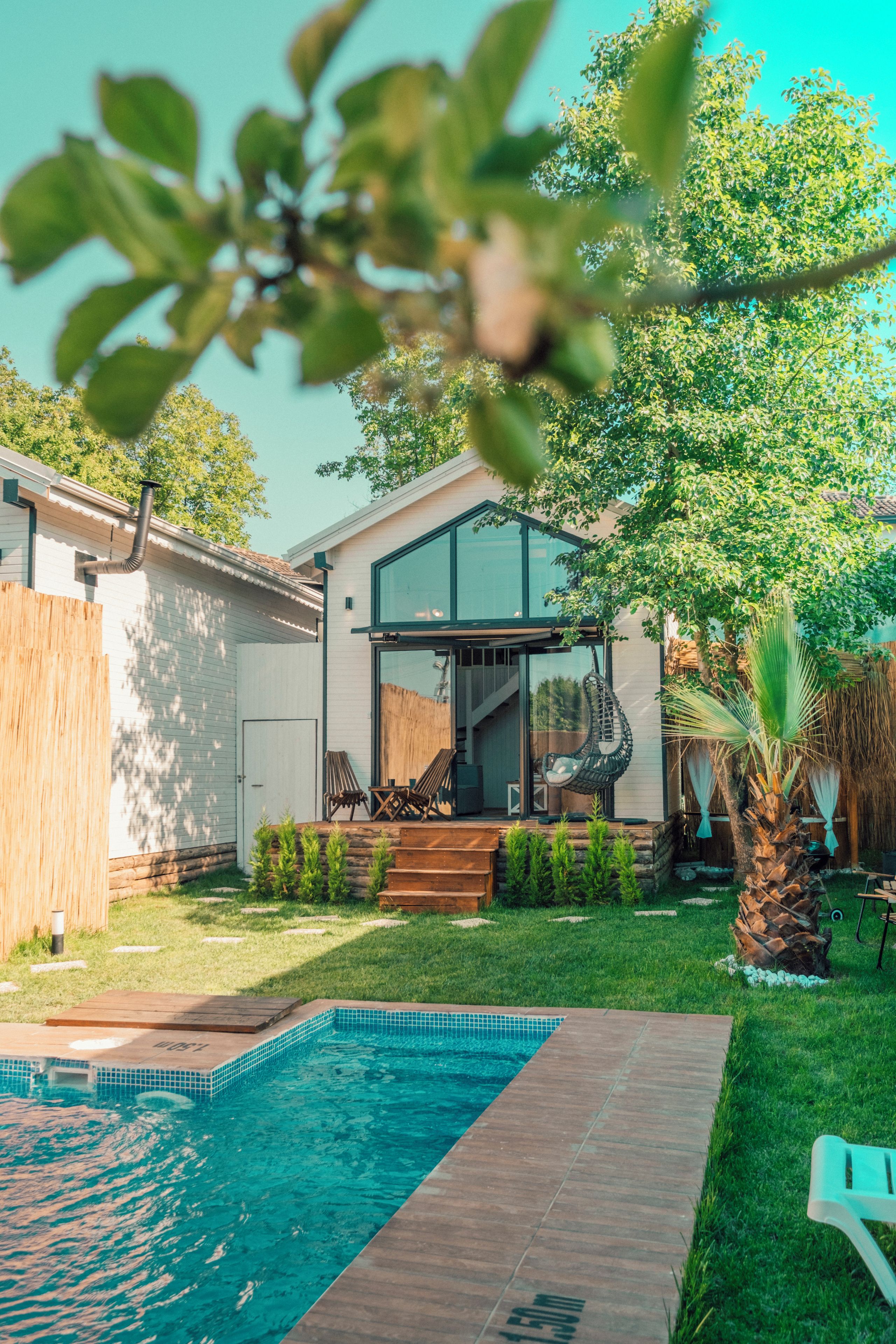 Una casa moderna con piscina, puerta de cristal y zona de patio con mobiliario exterior.