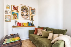 A cozy living room with a green sofa, a wooden coffee table with books, a radiator, and various framed artworks on the wall. - Modern 2BR Apartment near Leith Walk (Edinburgh)