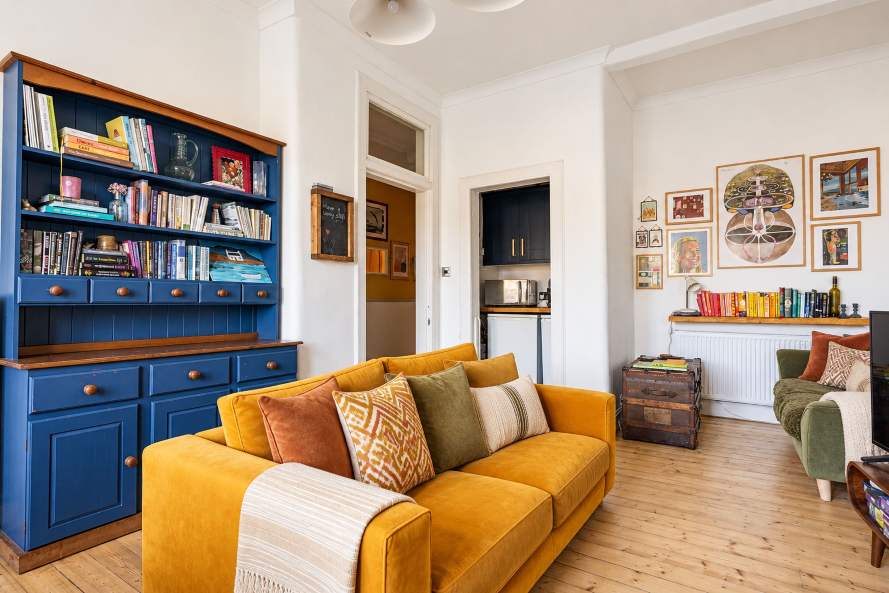 A living room with a yellow sofa, a blue bookshelf, and a green armchair.