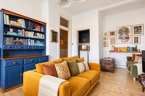 A living room with a yellow sofa, a blue bookshelf, and a green armchair. - Modern 2BR Apartment near Leith Walk (Edinburgh)