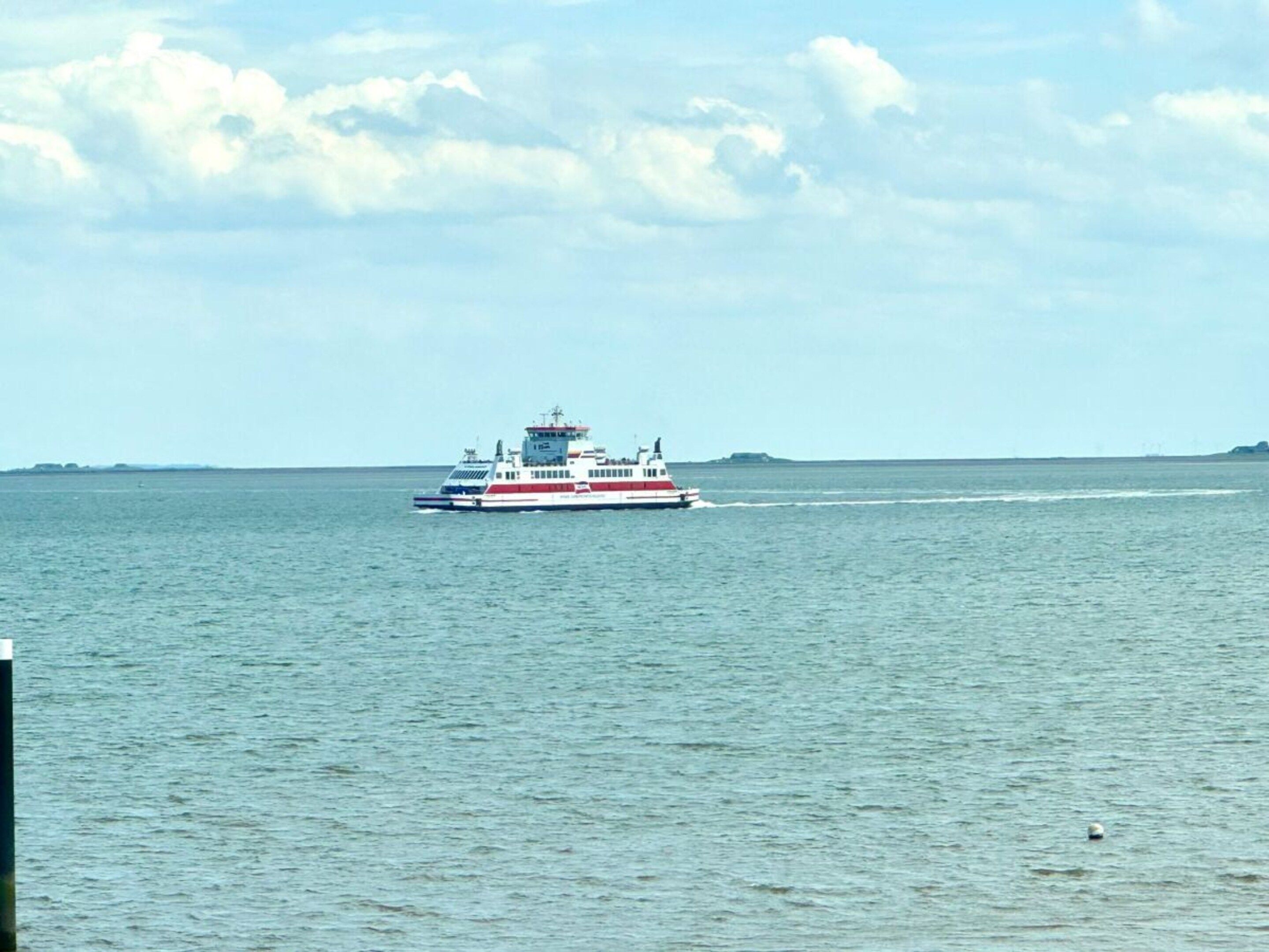 Un traversier navigue sur une étendue d’eau, avec une terre lointaine qui se profile à l’horizon.