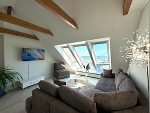 Un salón estilo loft con techo alto, tragaluces, televisor de pantalla plana, sofá y una lámpara decorativa.