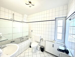 A bathroom with a bathtub, toilet, and a glass-enclosed shower area. - House With sea View - Apt. 3 (Wyk auf Foehr)