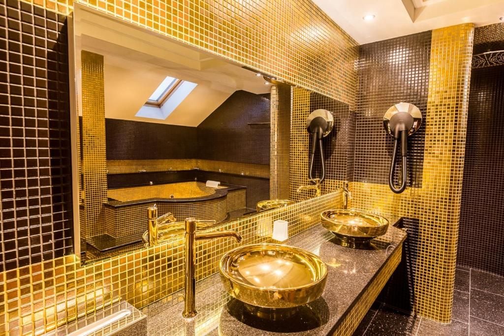 Un baño con un espejo grande, una bañera y dos lavamanos con detalles dorados.