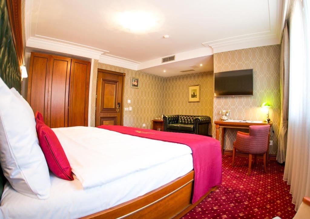 Habitación de hotel con una cama grande, un escritorio, una silla y un televisor en la pared.