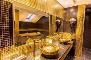 Un baño con tragaluz, una bañera y dos lavamanos con detalles dorados.