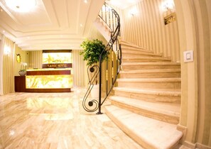 Eine Hotelhalle mit Marmorboden, einer Rezeption und einer Treppe mit Metallgeländer.