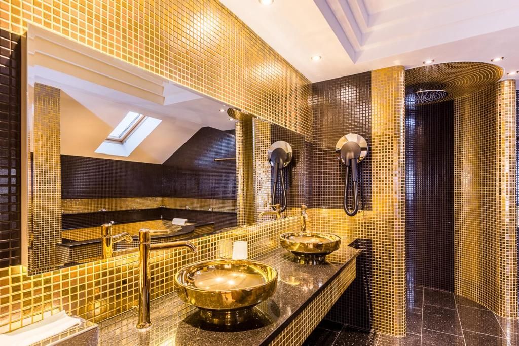 Une salle de bain luxueuse dotée d’une lucarne, de deux vasques avec des robinets dorés et d’un grand miroir.