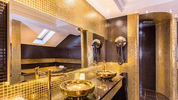 Une salle de bain luxueuse dotée d’une lucarne, de deux vasques avec des robinets dorés et d’un grand miroir.