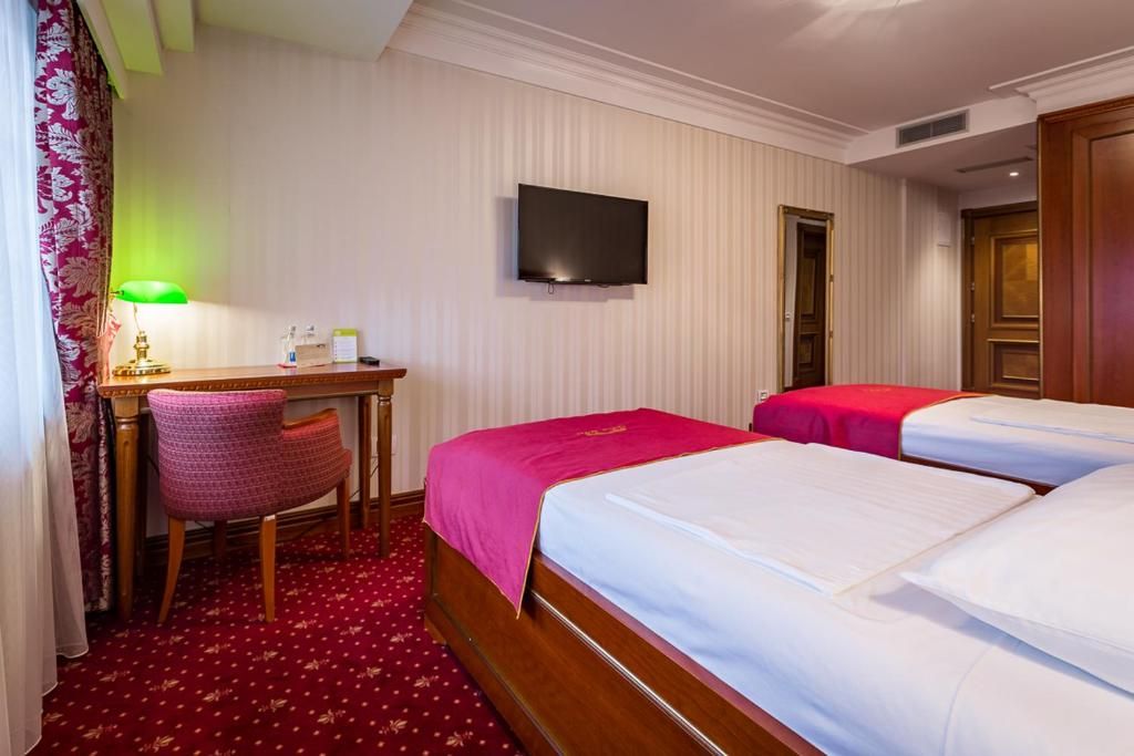 Una habitación de hotel con dos camas, un escritorio, una silla, un televisor y piso cubierto de alfombra roja.