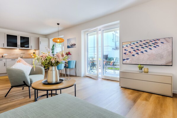 A modern living room with a dining area, a kitchen, and a large sliding glass door leading to an outdoor patio. - Beach Runner 4.2 | Sauna. Patio. Near the beach. (Kellenhusen)