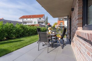 An outdoor patio with a table and chairs, a brick wall, and a view of neighboring buildings. - Beach Runner 4.2 | Sauna. Patio. Near the beach. (Kellenhusen)