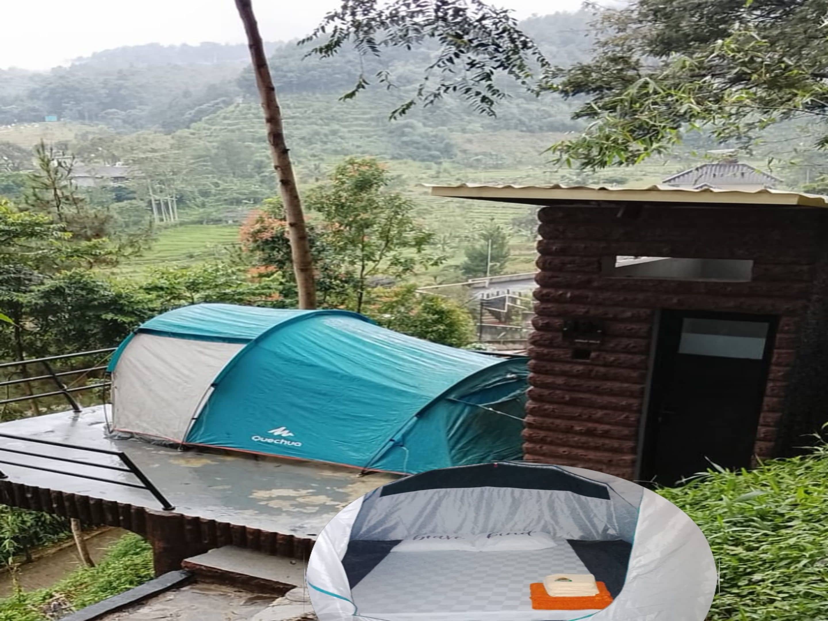 A tent with a sleeping area and a small brick structure, set against a hilly landscape.
