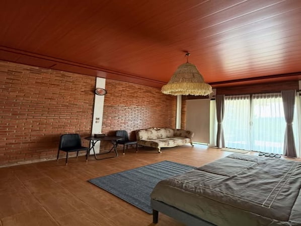 Une pièce avec un mur en briques, un plafond en bois, un lit, un canapé, une table à manger avec des chaises et un luminaire suspendu.