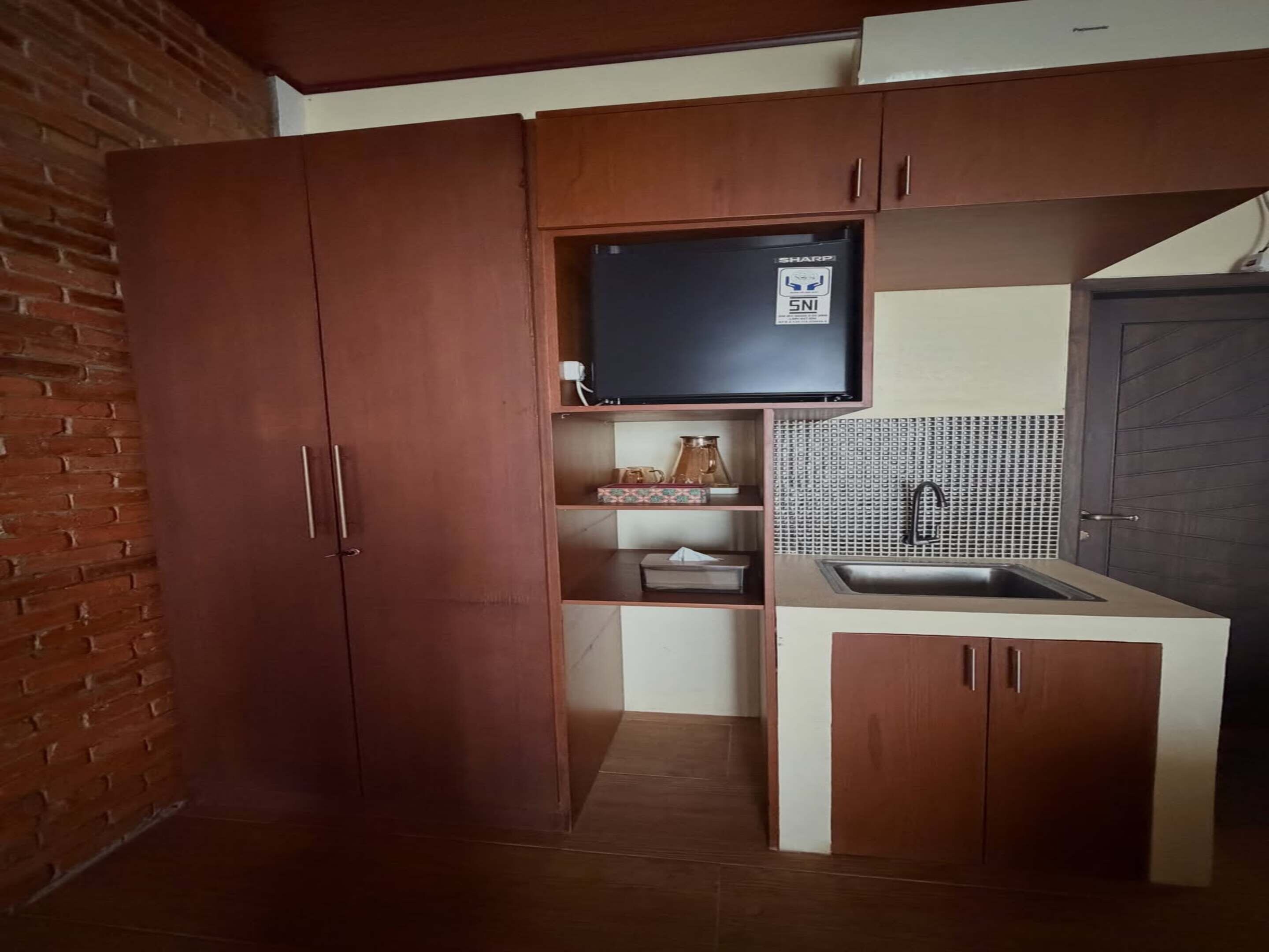 A compact kitchen with wooden cabinets, a built-in sink, and a television above the countertop.