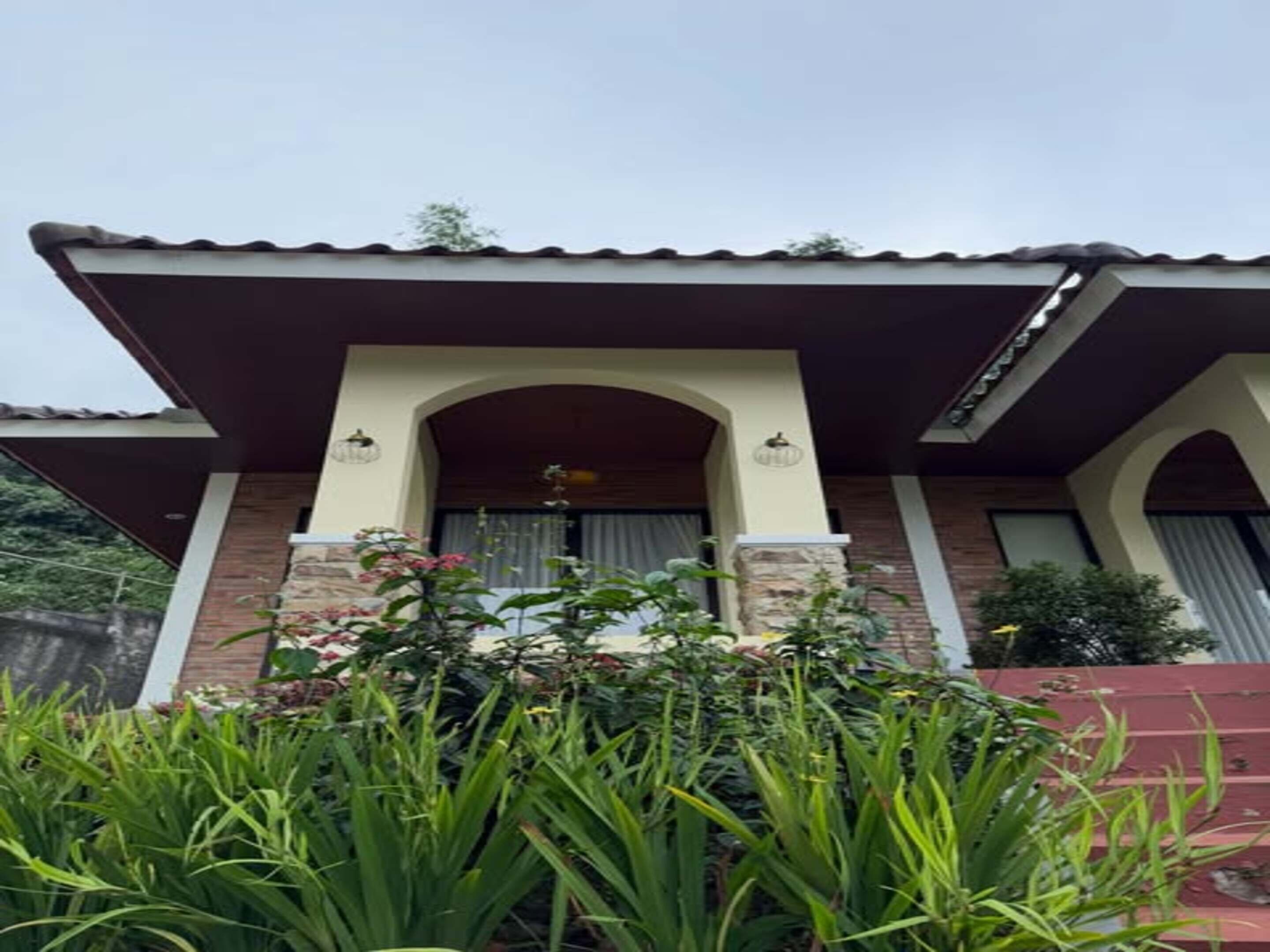 A house with a covered porch, stone pillars, and a tiled roof.