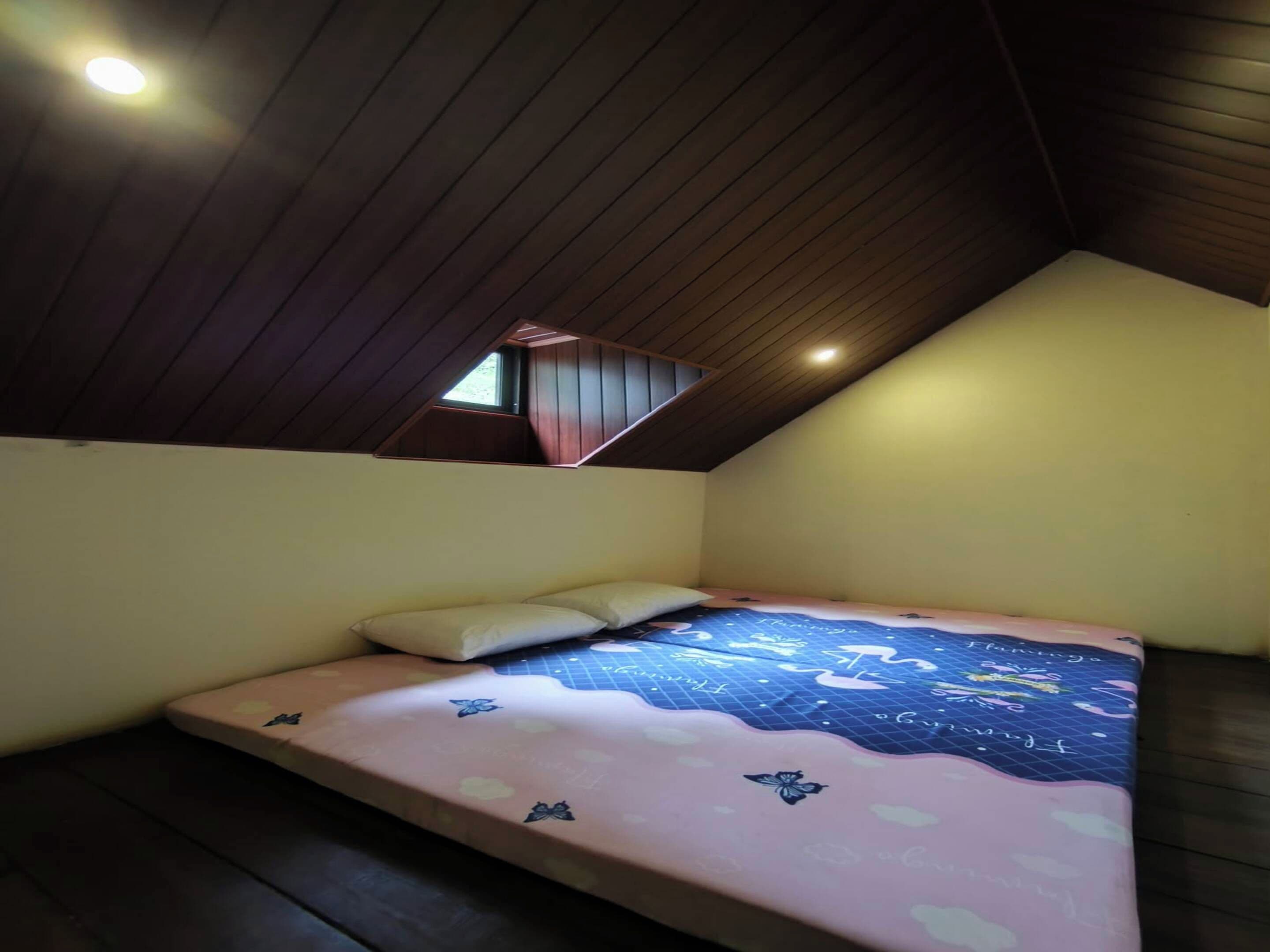 A bedroom with a sloped ceiling, a skylight, a bed with a floral bedspread, and a small window.
