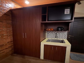 Une cuisine compacte dotée d’un évier encastré, de meubles en bois, d’un pare-feu en carreaux et d’un appareil électroménager noir posé sur le plan de travail.