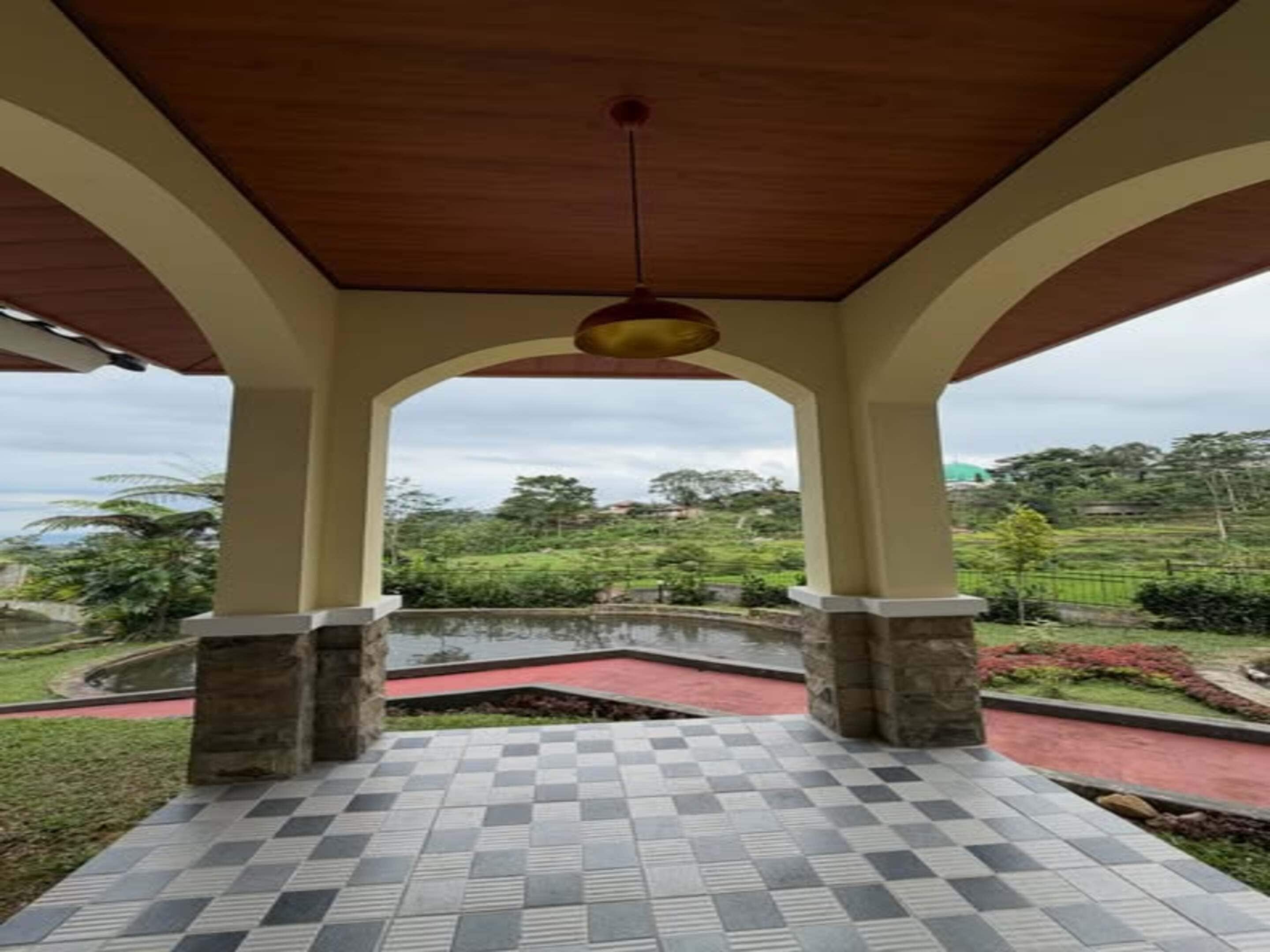 A covered outdoor area with a checkered floor, stone pillars, and a view of a green landscape.