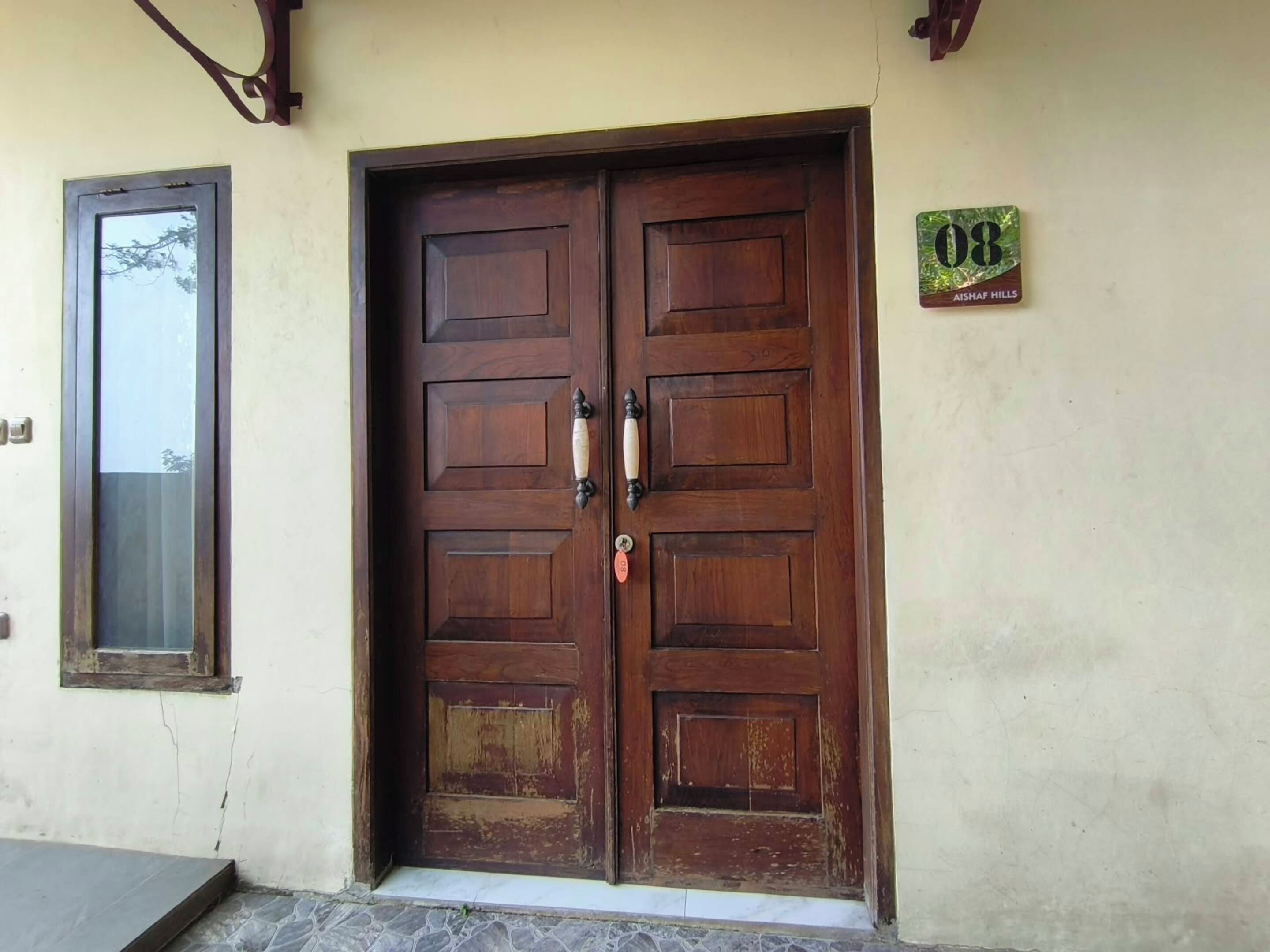 A wooden double door with a keyhole and a lock, a small window to the left, and a sign with the number '08' on the wall.