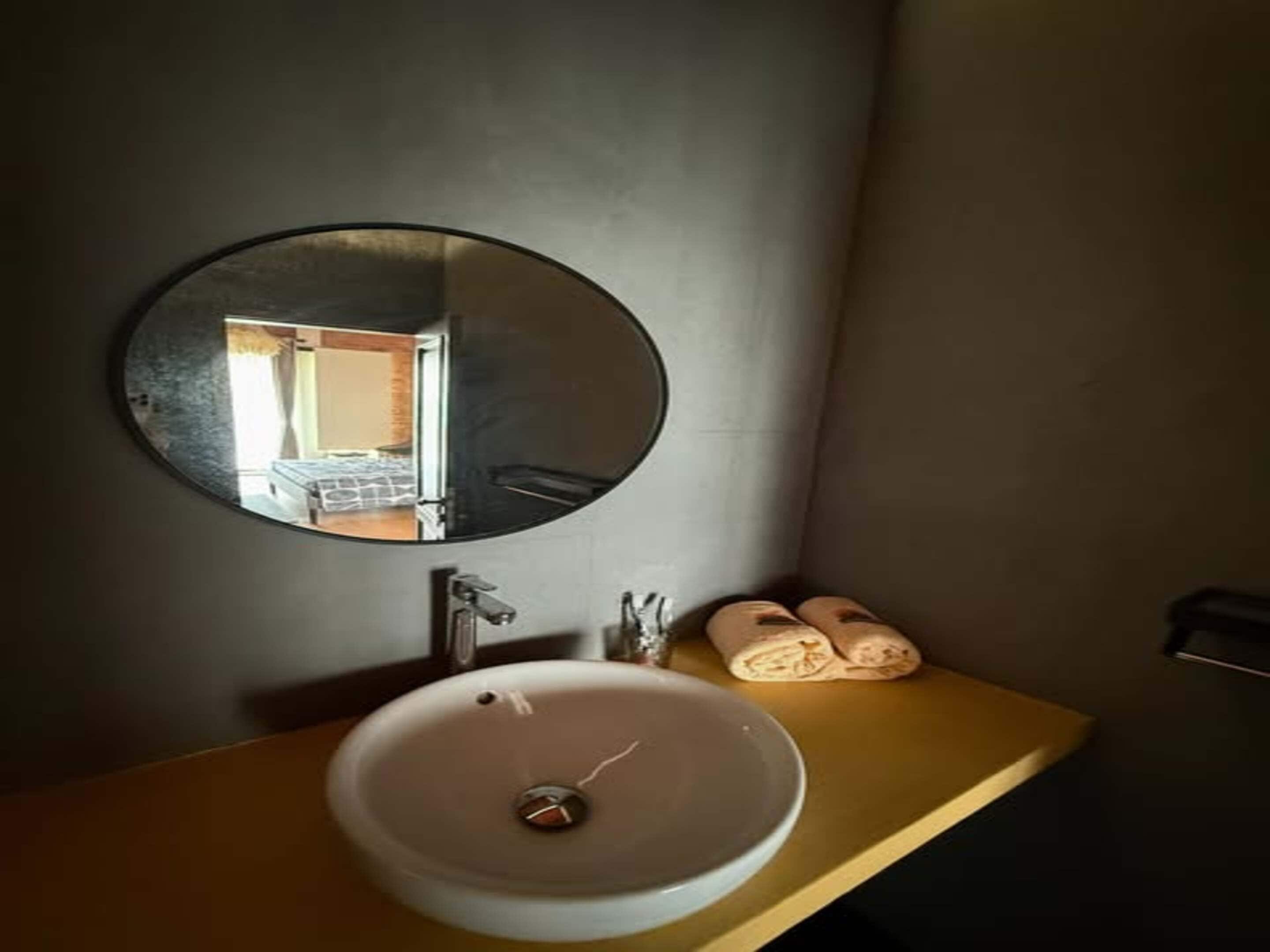 Een badkamer met een ronde spiegel, een wastafel en een handdoekhouder.