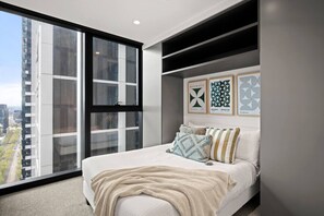 A modern bedroom with a large window, a bed with multiple pillows, and a wall with framed artwork. - City View 2 Bedroom with Pool (Melbourne)