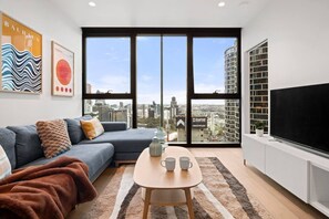 A modern living room with a sectional sofa, a coffee table, and a large TV. - City View 2 Bedroom with Pool (Melbourne)