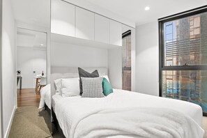 A modern bedroom with a large bed, a desk, and a window with a city view. - Lavish 2 Bedroom City Retreat (Melbourne)