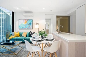 A modern living room with a sofa, coffee table, and dining area with chairs. - Lavish 2 Bedroom with Sauna (Melbourne)