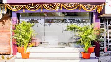 A storefront with a purple facade, a glass entrance, and two potted plants on the steps.