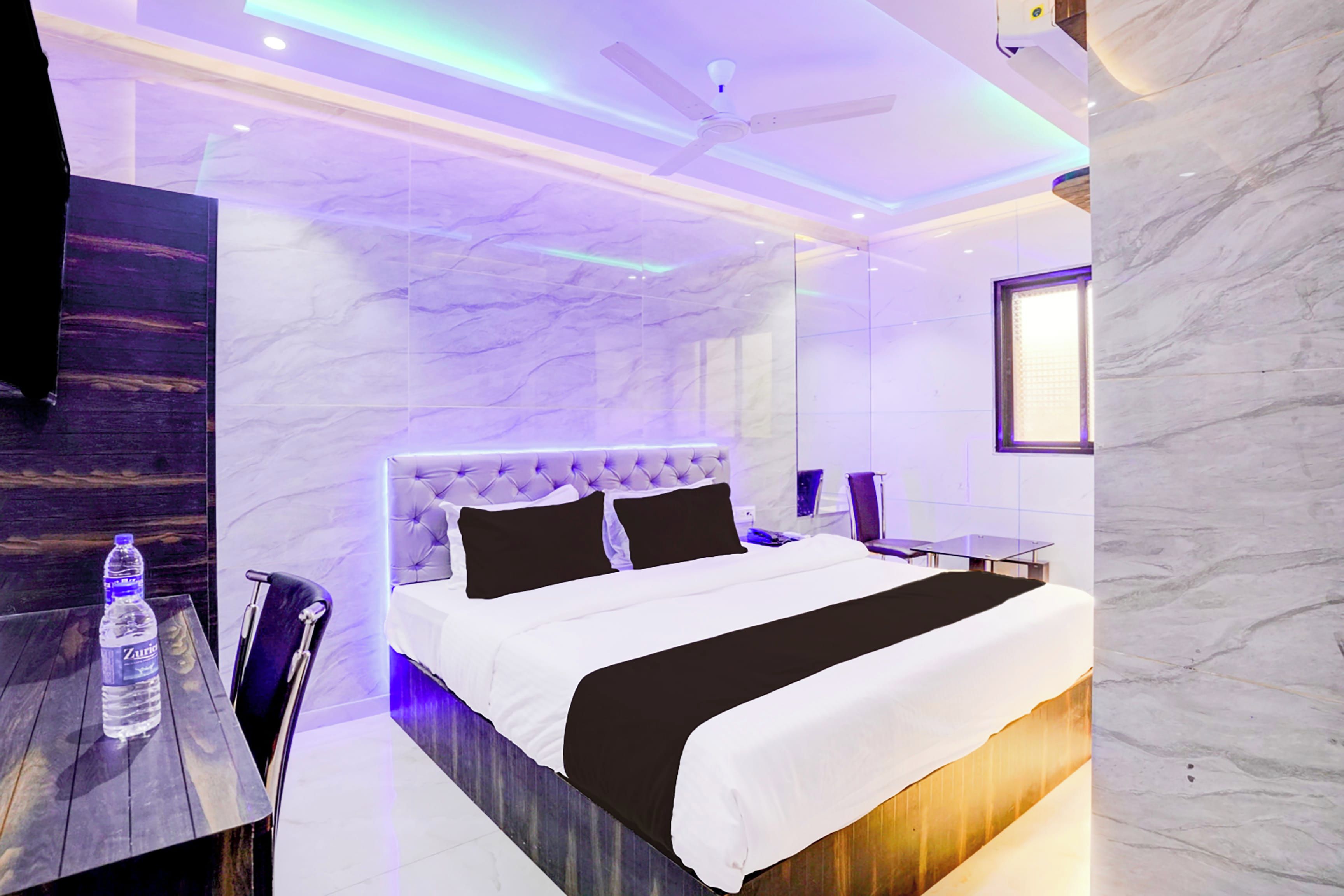 A modern hotel room with a marble wall, a tufted headboard, a large bed, a bedside table, and a water bottle.