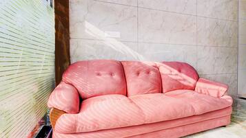 A pink sofa in a room with marble walls and a window with blinds.