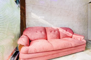 Un sofá rosa en una habitación con paredes de mármol y una ventana con persianas.