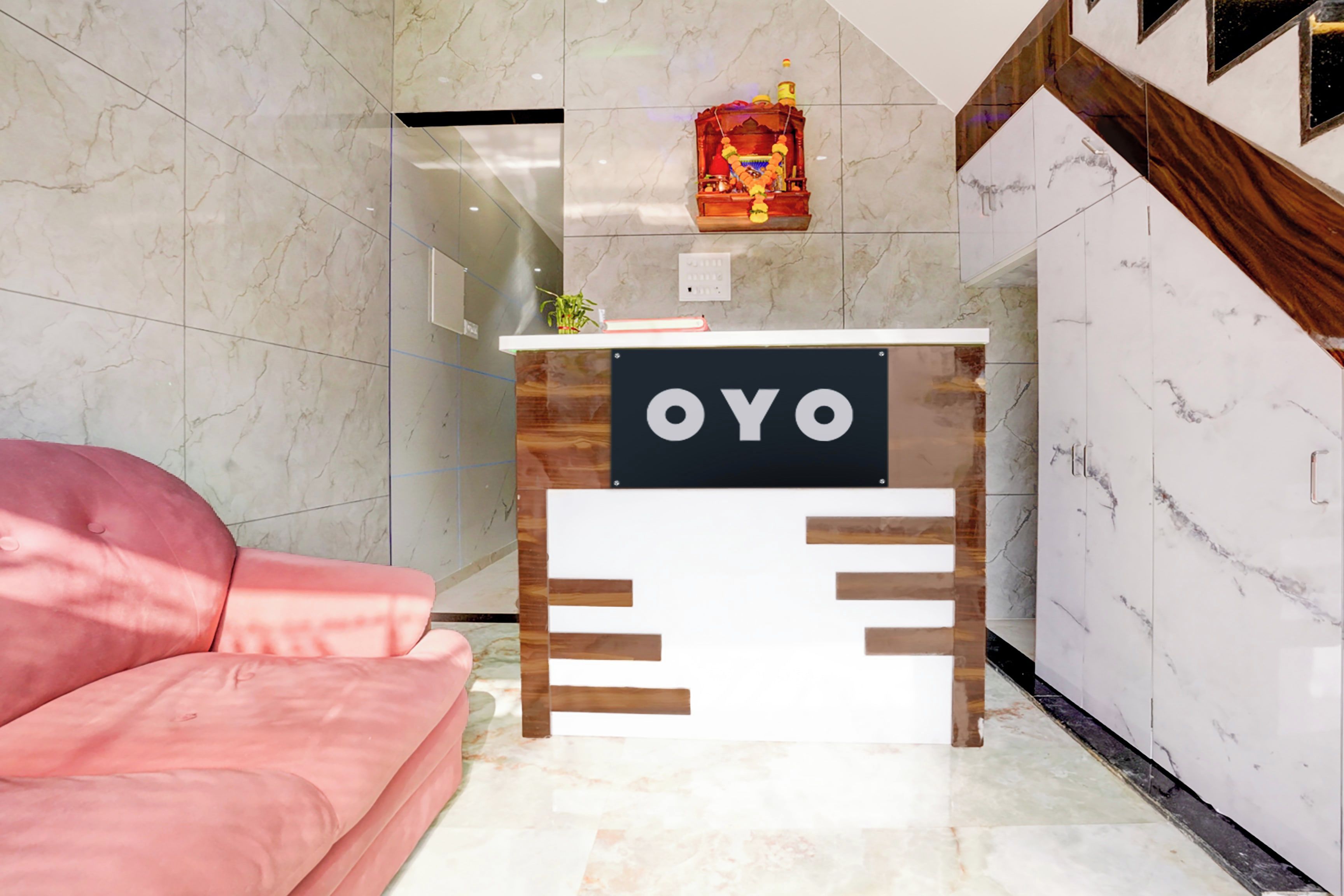 A reception desk with a sign that reads 'OYO' in a modern hotel lobby with marble walls and a pink sofa.