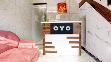 A reception desk with a sign that reads 'OYO' in a modern hotel lobby with marble walls and a pink sofa.