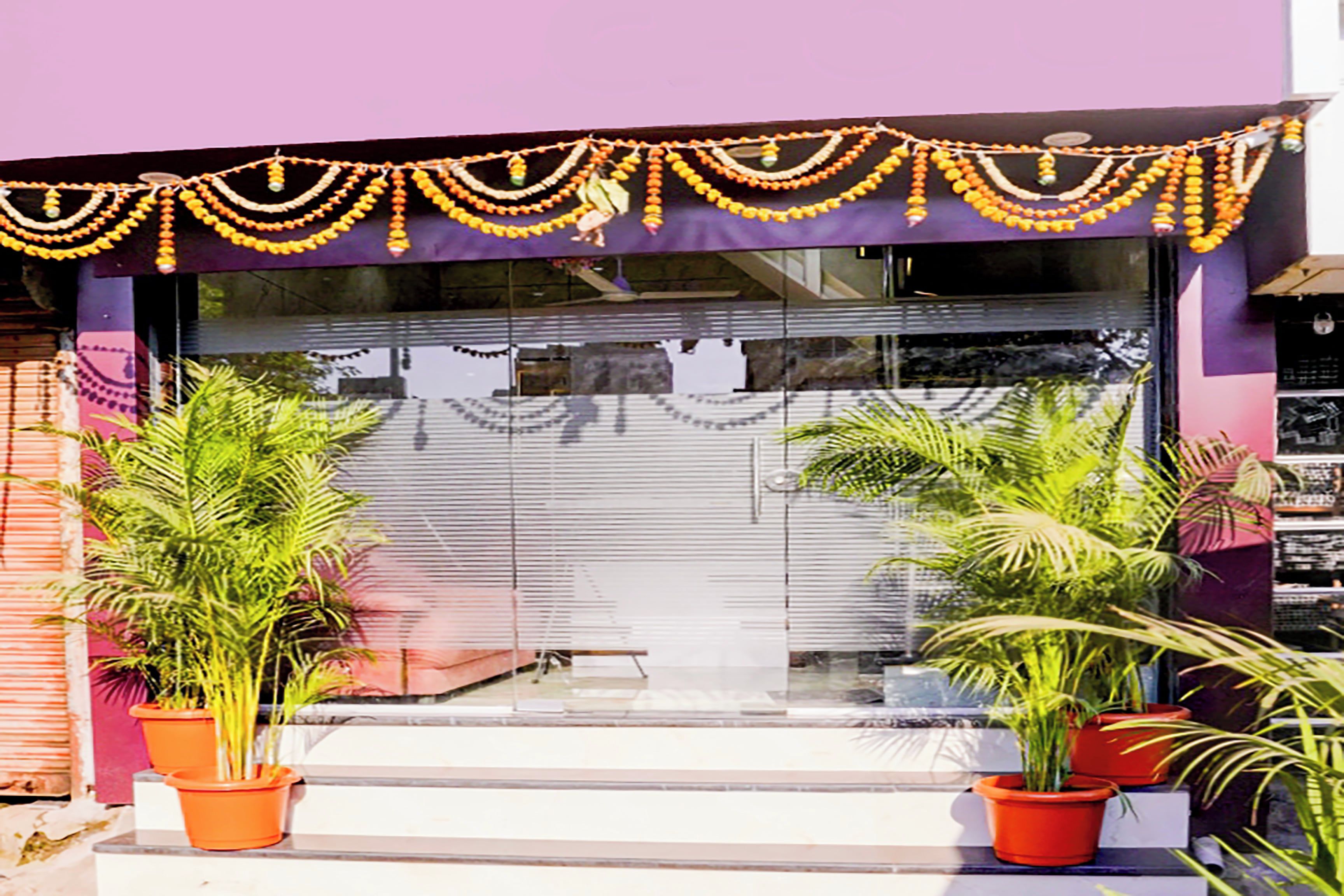 A storefront with a purple awning, potted plants, and a closed glass door.