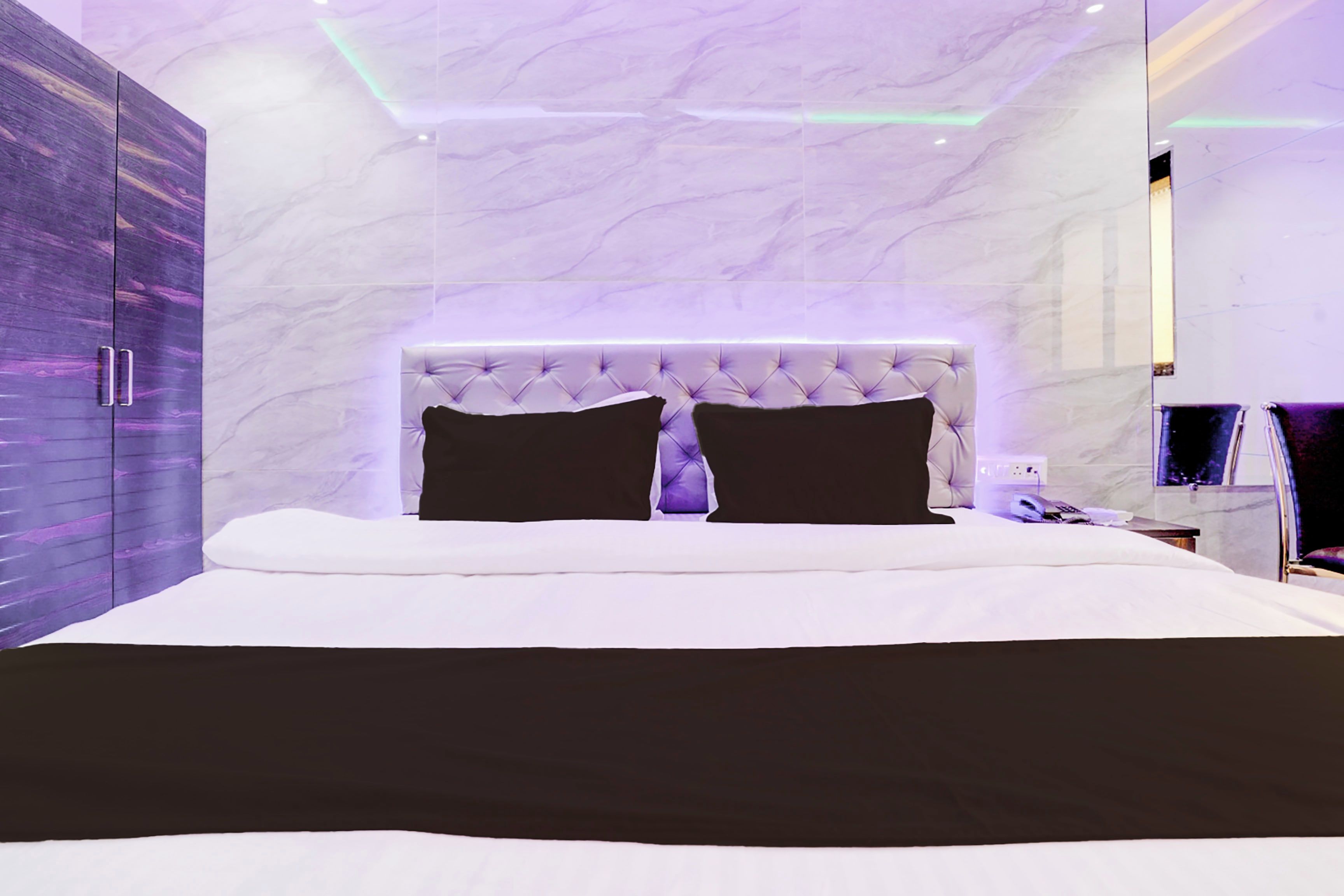 A modern bedroom with a marble headboard, a large bed, and a wardrobe with a purple finish.