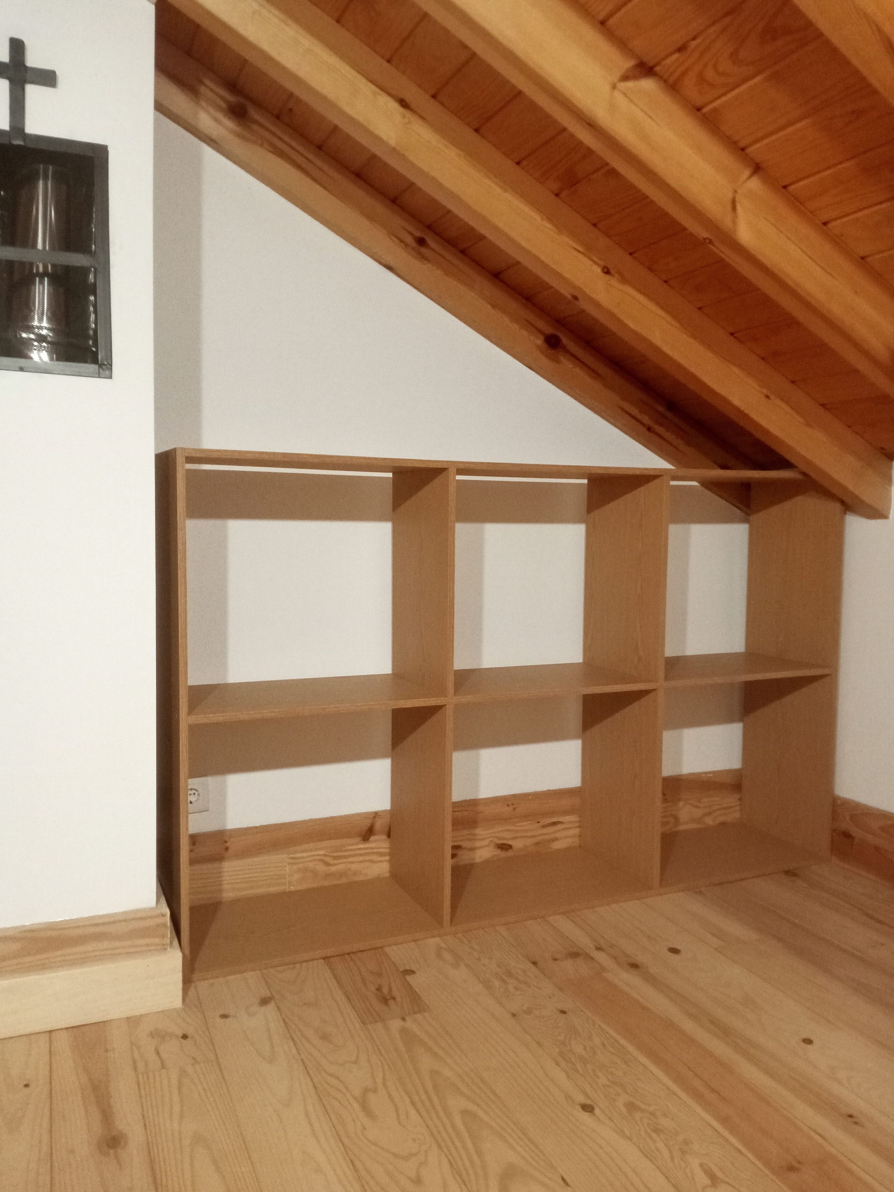 Une pièce avec un plafond en pente, un plancher en bois et une bibliothèque intégrée le long d’un mur.