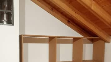 A room with a sloped ceiling, wooden flooring, and a built-in shelving unit against the wall.