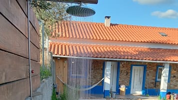 A rustic outdoor area with a wooden pergola, a stone wall, and a tiled-roof building.
