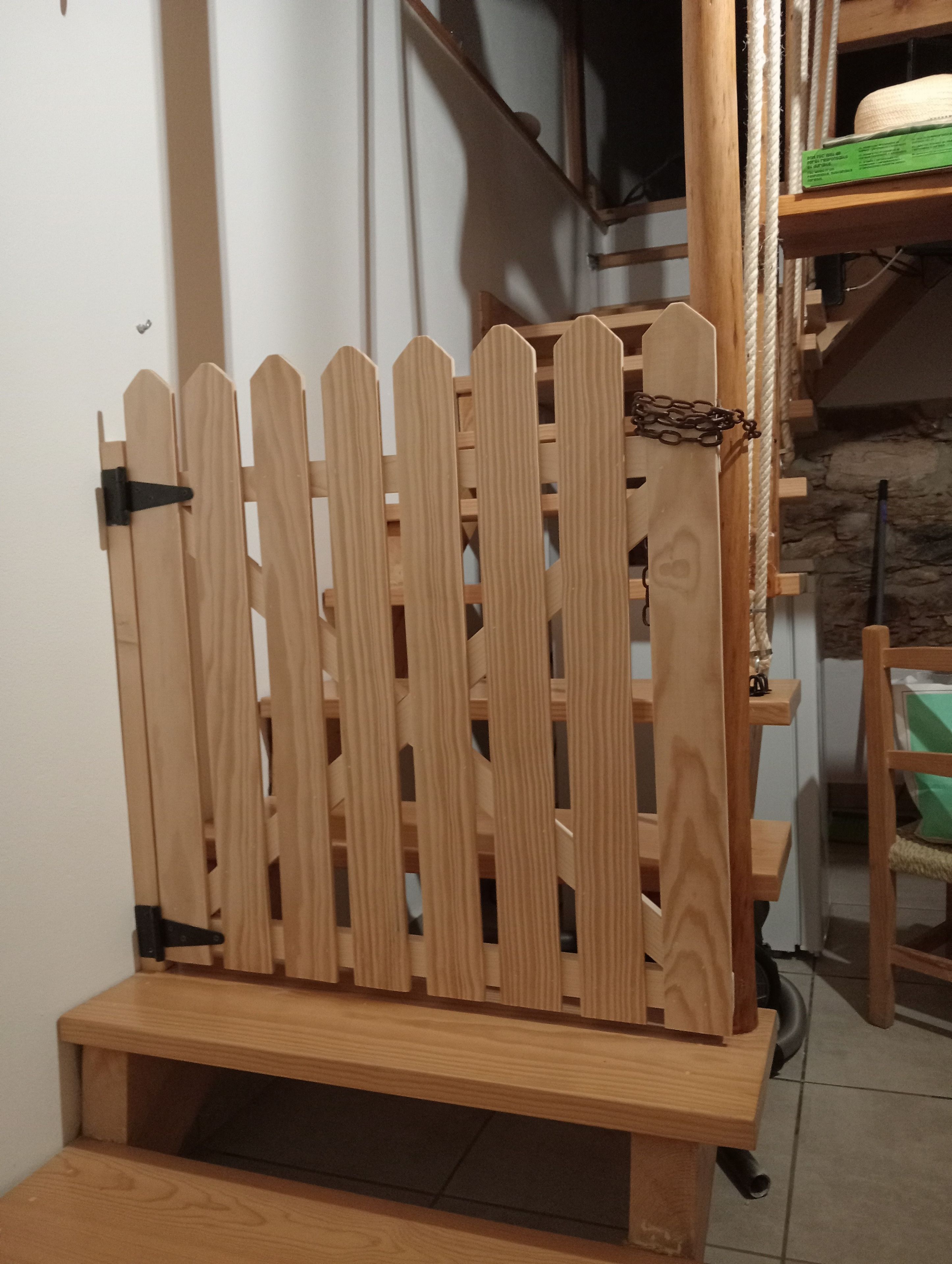 A wooden bench with a slatted backrest and a lower shelf, situated in a room with a stone wall and a wooden shelf in the background.
